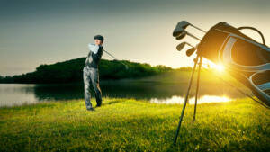 golf bag in foreground, golfer teeing off in back ground at sunset