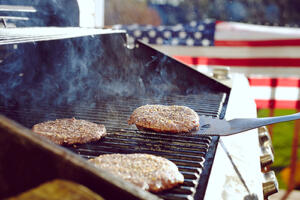 hamburgers cooking on a grill in front of American Flag