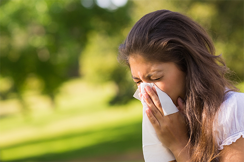 woman outside sneezing into a tissue 