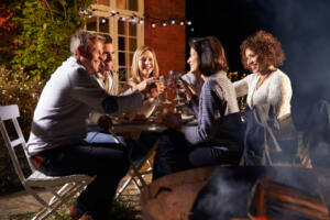 mature friends enjoying outside dinner party by fire pit