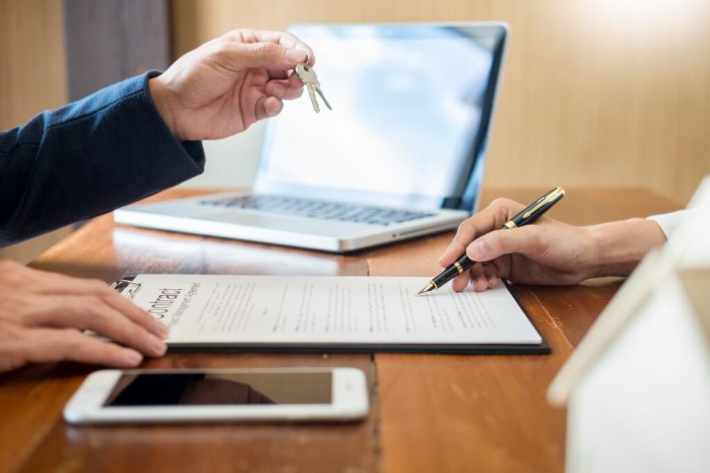 Real estate agent handing keys to person signing housing contract