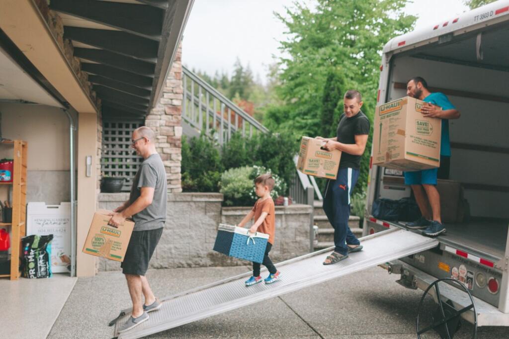 Group of three men and a little boy carrying moving boxes out of a rental truck