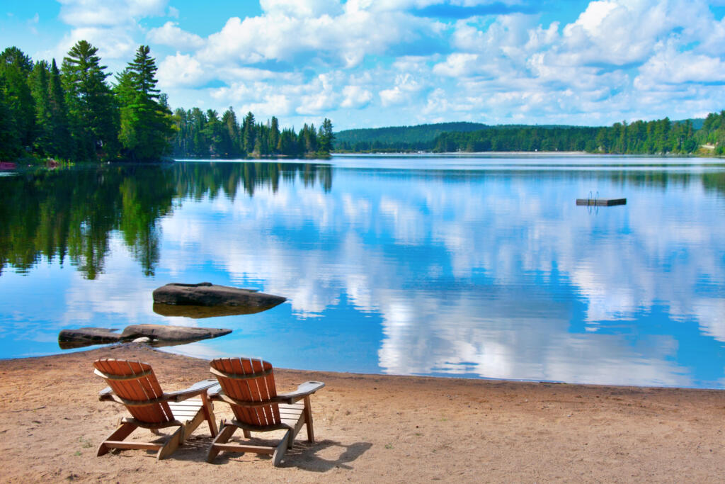 two wooden deck chairs on the shore of Douglas Lake with clouds reflecting on the water