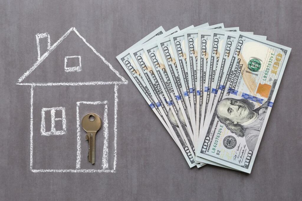 Chalk drawing of a house with a key in the doorway next to a fanned out stack of $100 bills the hidden costs of buying a lake home