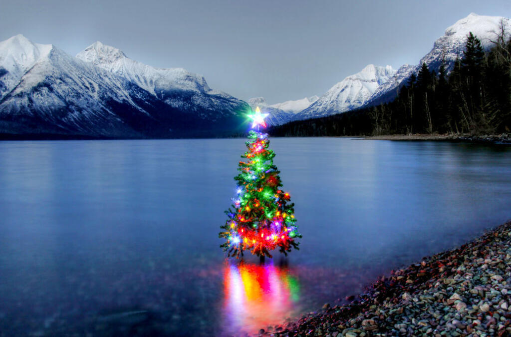 Lit Christmas tree in lake surrounded by snow capped mountains