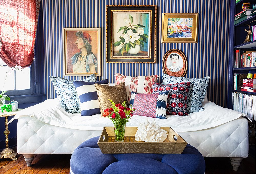 Striped navy blue wallpaper with paintings and vibrant pillows on daybed interior design trend