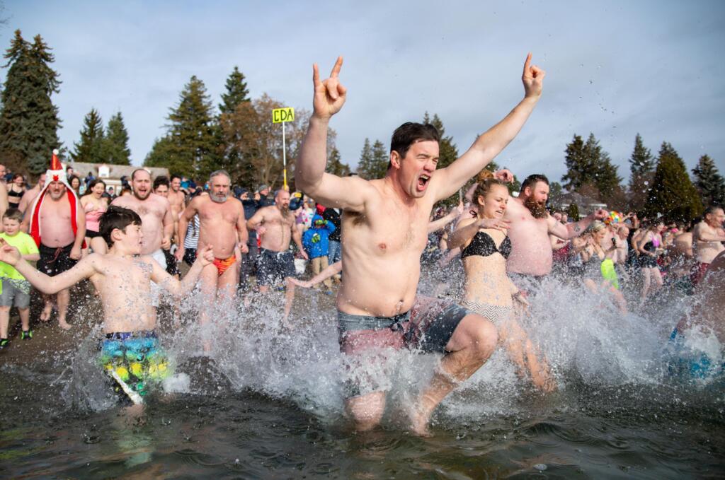 Man raising rock on symbols in air running into lake with large crowd behind him