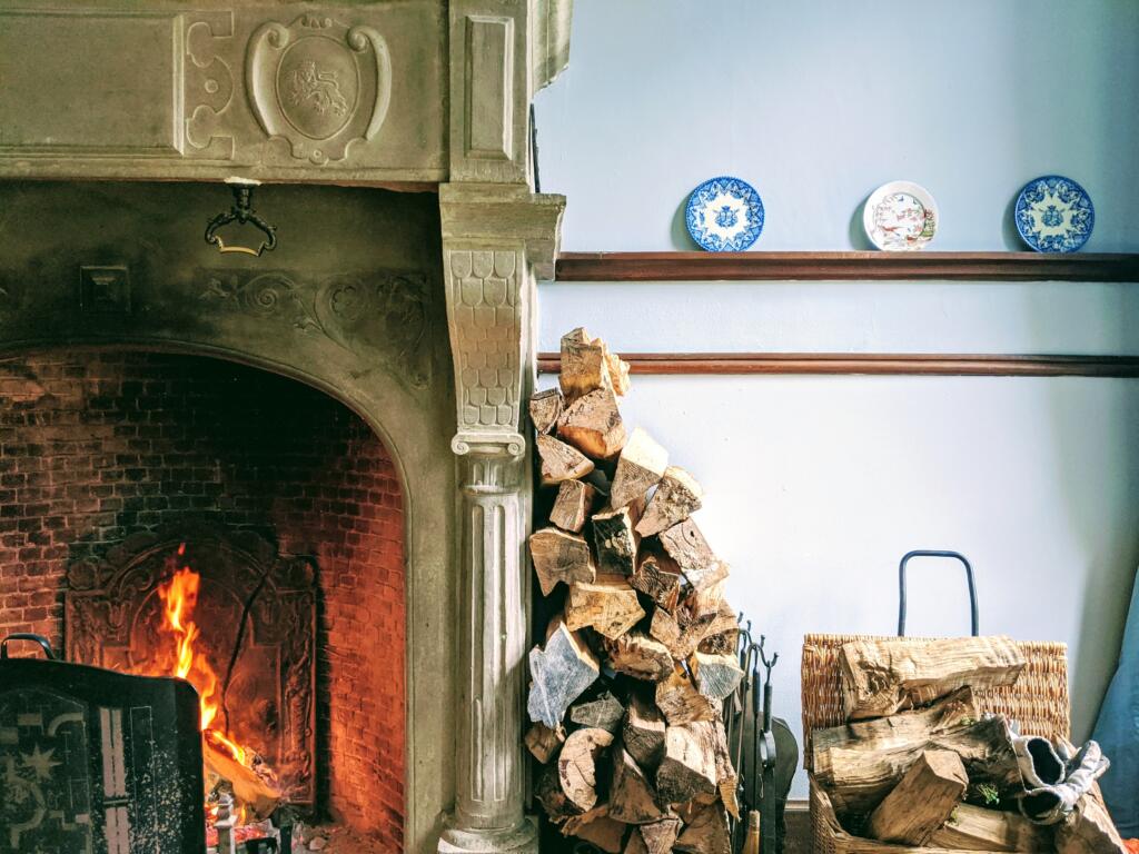 Pile of chopped firewood leaning  against lit wood fireplace