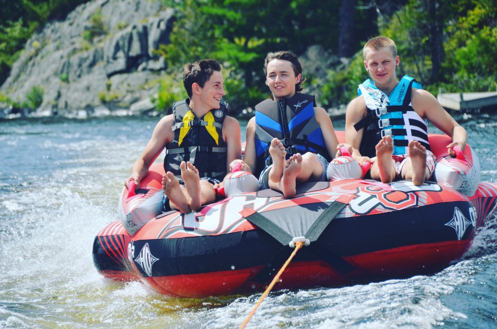 three boys sitting on raft at lake