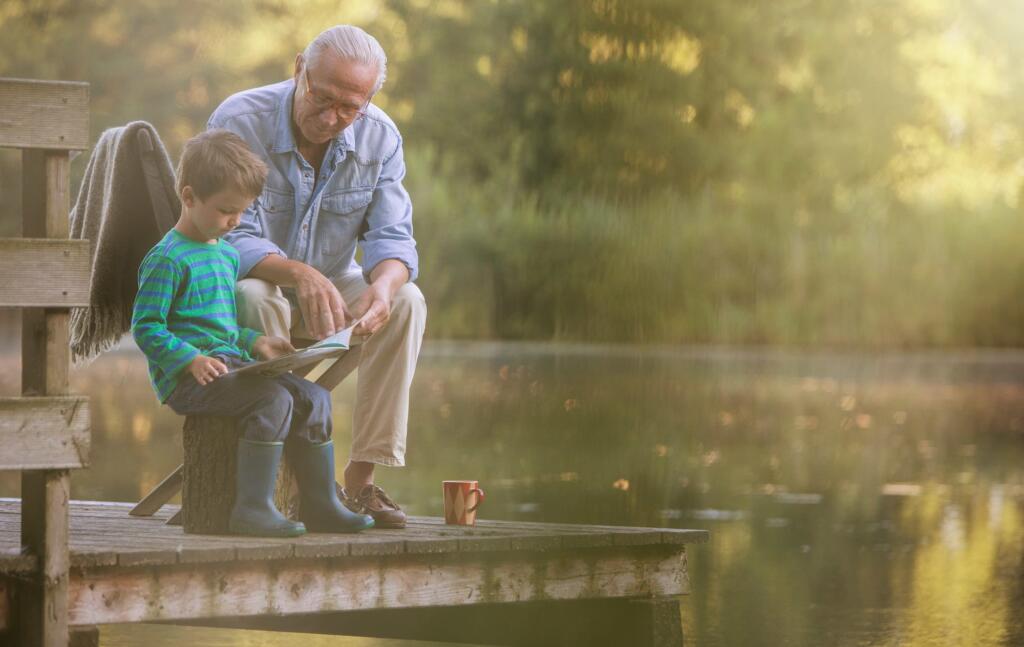 Grandfather reading with grandson at lake