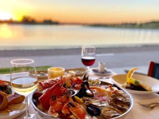 plates of seafood and fish with glasses of wine overlooking lake at sunset