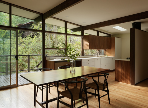 Remodeled mid-century modern kitchen with walnut and white laminate cabinetry, a handcrafted dining table, and outdoor deck in the woods surrounding Lake Washington