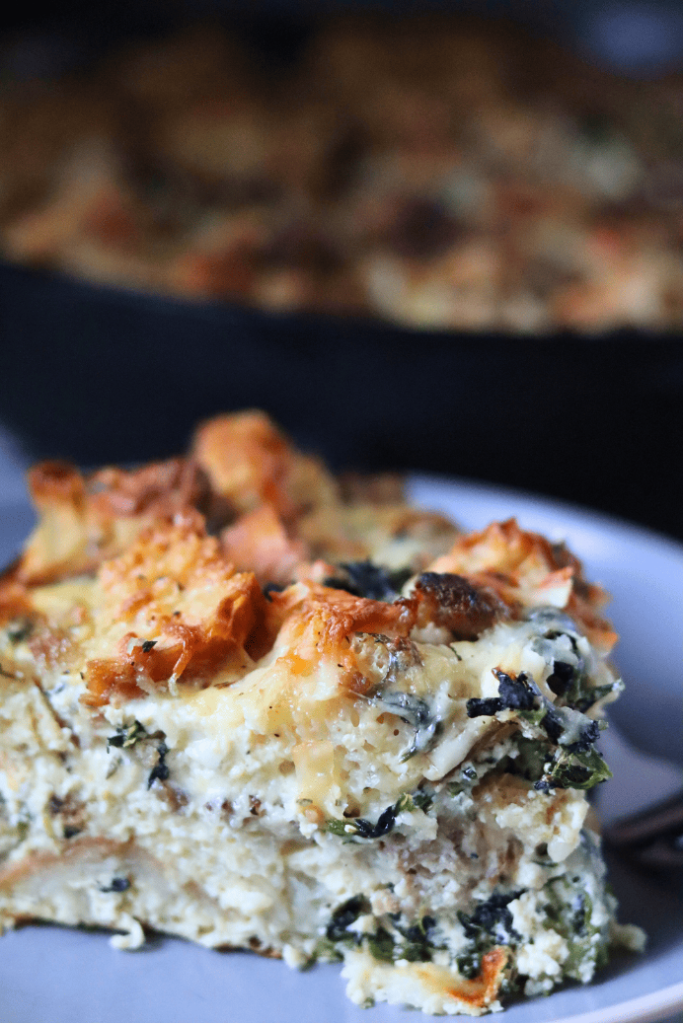 Savory Spinach and Sausage Strata on a blue plate with cast-iron skillet blurred in background