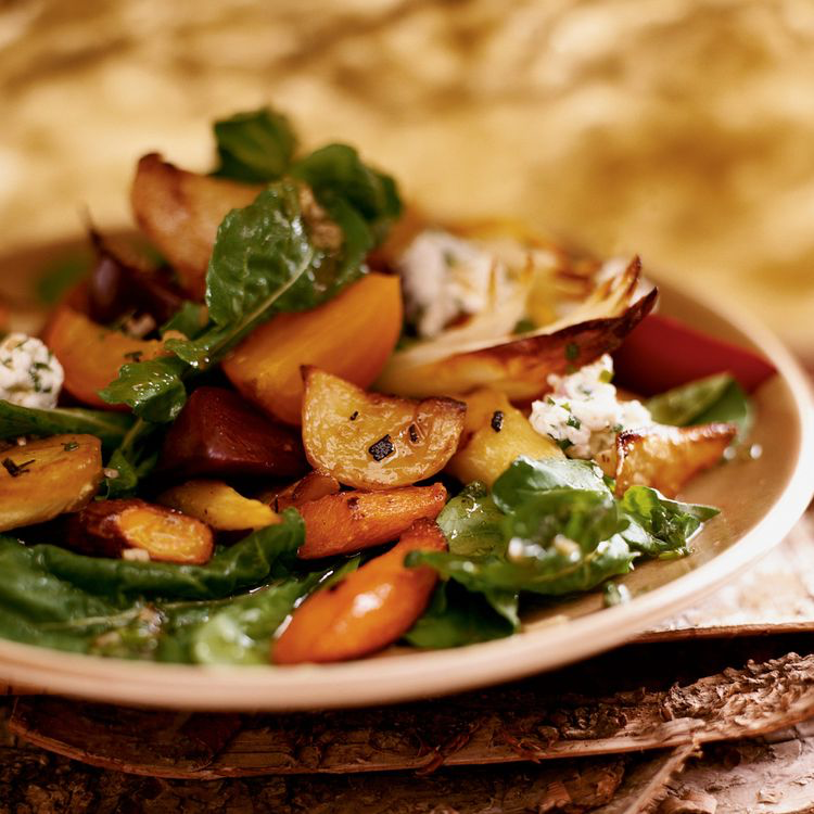 Honey-Roasted Root Vegetable salad with sage and goat cheese over a bed of arugula dressed in vinaigrette on a salad plate.