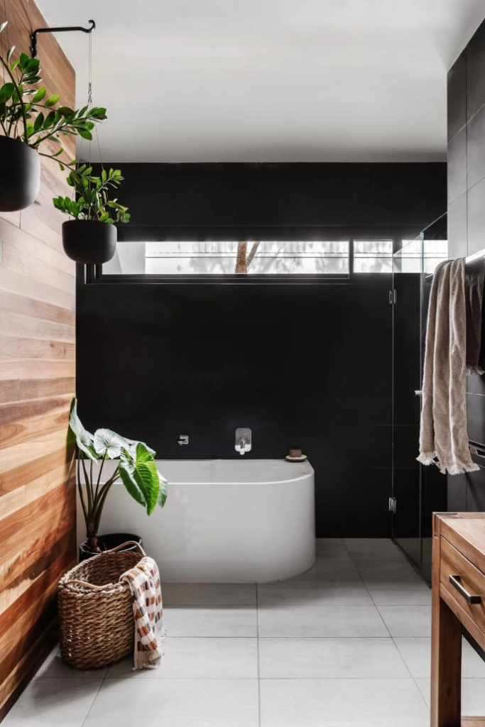 hanging plants and a potted plant in black containers in a black bathroom with natural wood walls and white tub