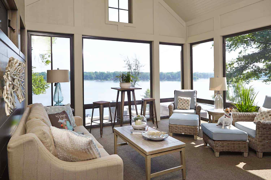 Sunroom of home on Reeds Lake in East Grand Rapids, MI, with upholstered seating, cushioned wicker seating, lake views, neutral decor, and a Jack Russell terrier