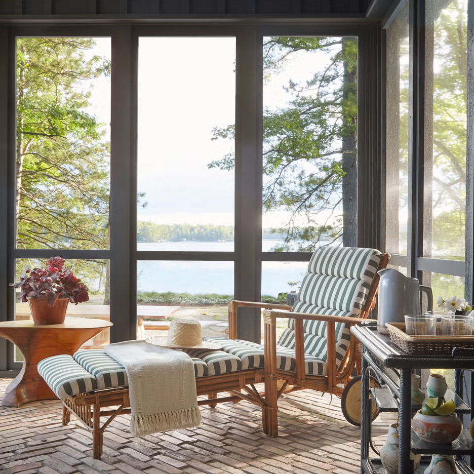 Southeaster Lake region sunroom with bamboo chaise lounge, striped cushion, bar cart, organic wooden table, brick floors, and splendid lake views