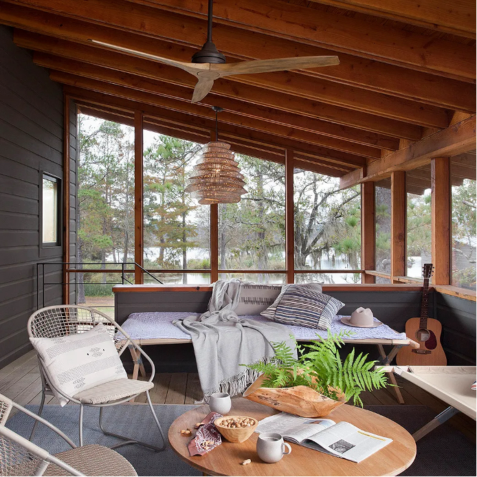 Sunroom and sleeping porch in the Deep South with simple cots, oudtoor chairs, wooden coffee table, ceiling fan, guitar in corner