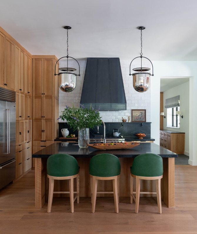 Black soapstone countertop and shelf surfaces in a kitchen with white Zellige tile blacksplash contrasting black range hood, silver mercury-glass pendant lights with black hardware